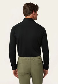 Schwarzes Langarmshirt mit Knopfkragen und -manschetten, kombiniert mit olivgrünen Hosen mit elastischem Bund und Gesäßtaschen.