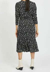 Musta mekko, jossa on valkoinen abstrakti kuvio, pitkät hihat ja röyhelöhelma, yhdistettynä kreeminvärisiin nilkkabootseihin. Silkkinen kangas