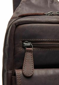 Borsa in pelle marrone con una tasca con zip e zip argentato, e una finitura testurizzata. Include un accento in pelle cucita per una presa sicura.