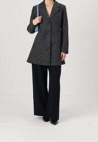 Grå kappa i ullblandning med notchad krage, två knappar och utsvängd fåll, kombinerad med svart högmidjad byxa med vida ben och en ljusblå väska.