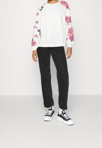 Felpa crema con motivi floreali rosa sulle maniche, abbinata a jeans neri a gamba dritta e sneakers bianche e nere.