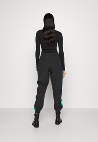 Svarta joggers med elastisk midja, avsmalnande muddar och kontrasterande blå sidosträck med gröna logotypdetaljer. Materialet verkar vara lätt.