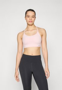 Sutiã desportivo rosa claro com alças finas, textura suave e um design ajustado. Combinado com leggings pretas de cintura alta com um acabamento sem costuras.