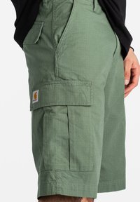 Bermudas cargo verdes hechas de tejido ligero con múltiples bolsillos, incluido un gran bolsillo cargo en el lateral y detalles de costura.