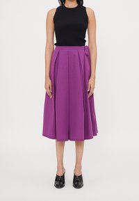 Top negro de canalé combinado con una falda plisada morada hasta la rodilla, con un detalle de lazo lateral, llevada con unos mule negros de tacón.