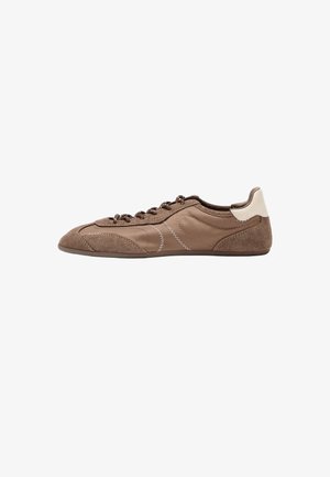 Flacher brauner Sneaker mit gemischten Velours- und glatten Texturen, dunklen Schnürsenkeln, hellem Fersenlasche und Zickzack-Nahtdetail auf weißem Hintergrund.