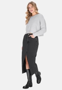 Szary dziany sweter o kroju cropped, czarna denimowa spódnica z przednim rozcięciem oraz wysokie czarne kozaki z klamrami. Prosty, nowoczesny wygląd.