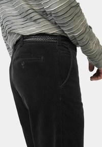 Schwarze Cordhosen mit vertikaler Rippstruktur; ausgestattet mit Taschen, einem Knopfverschluss und einem gewebten schwarzen Gürtel für zusätzliche Details.