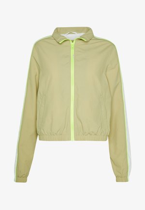 Ljusgrön vindjacka med dragkedja fram, elastisk midja och vita sidremsor. Tillverkad av ett mjukt, lätt material.