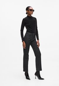 Zwarte coltrui met een subtiele glans, gecombineerd met hoogsluitende, gemarmerde zwarte broek en gepatenteerde leren puntige hakken.