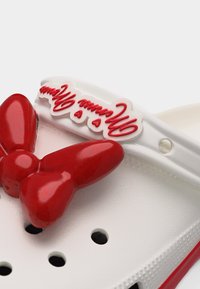 Λευκό παπούτσι με διακόσμηση κόκκινου φιόγκου και κόκκινα καλλιγραφικά γράμματα στο λουράκι που γράφουν "Minnie Mouse" με μικρές λεπτομέρειες καρδιάς.