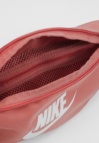 Röd zippered pouch med meshfickor inuti, tillverkad av hållbart material. Har Nike-logotyp i vitt. Texturerat tygutsida.