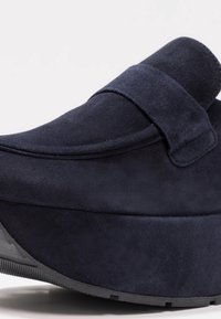Tmavě modré semišové slip-on boty s silnou podešví a širokým páskem přes přední část, vyfotografované na bílém pozadí.