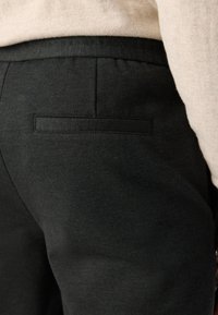 Pantalons noirs avec une texture lisse et une poche arrière unique. Comprend une taille ajustée, des bords ourlés et des détails de design minimalistes.