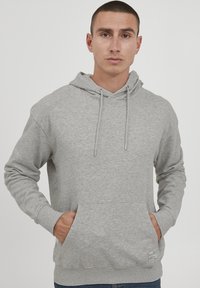 Sudadera gris con capucha ajustable, bolsillo tipo canguro en la parte delantera y puños de canalé. La tela parece suave con un acabado ligeramente texturizado.