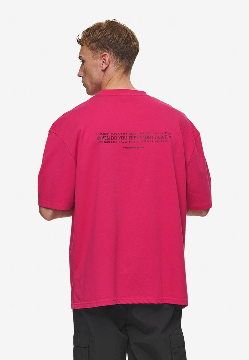 Pink cotton t-shirt with a relaxed fit, featuring text print on the back. Short sleeves and crew neckline. No visible patterns or accents.