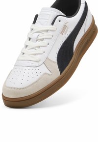 Baskets blanches avec un bout en daim beige et une bande latérale bleu marine. Caractéristiques : détails perforés, lacets plats et semelle en gomme.