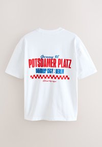 Biała bawełniana koszulka z czerwoną i niebieską grafiką: "Niemcy 95 Potsdamer Platz Daimler City: Berlin" z kraciastym wzorem na dole.