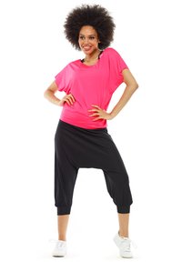 Roze, losse top gecombineerd met zwarte harem broek. De outfit heeft een ontspannen ontwerp en wordt aangevuld met witte sneakers.