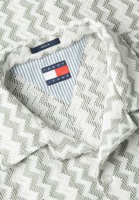 Chemise blanche et grise à motif zigzag avec col, étiquette Tommy Jeans à l'intérieur du col et étiquette de taille normale au-dessus.