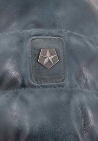 Dunkelblaues Leder mit einem hexagonalen Patch, auf dem ein silberner Stern geprägt ist. Die Oberfläche zeigt eine subtile, strukturierte Oberfläche.