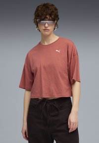 Beskarret, kortærmet t-shirt i rust med et subtilt Puma-logo. Ved siden af mørke bukser ser stoffet blødt og let ud.
