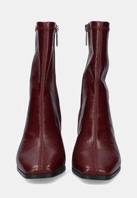 Botas de tobillo de cuero burdeos con punta delgada y afilada, cremalleras laterales y detalles de costura vertical. Textura suave y silueta elegante.
