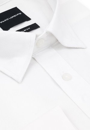 Biała bawełniana koszula o średnim kroju, z ostro zakończonym kołnierzykiem, zapięciem na guziki i widocznymi etykietami marki. Gładka tekstura z detalami przeszyć.