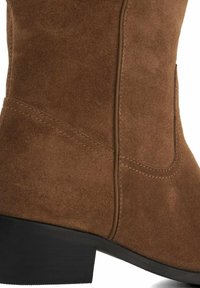 Bottine en daim marron avec une finition texturée, bout arrondi, petit talon noir et couture ton sur ton le long des coutures latérales.