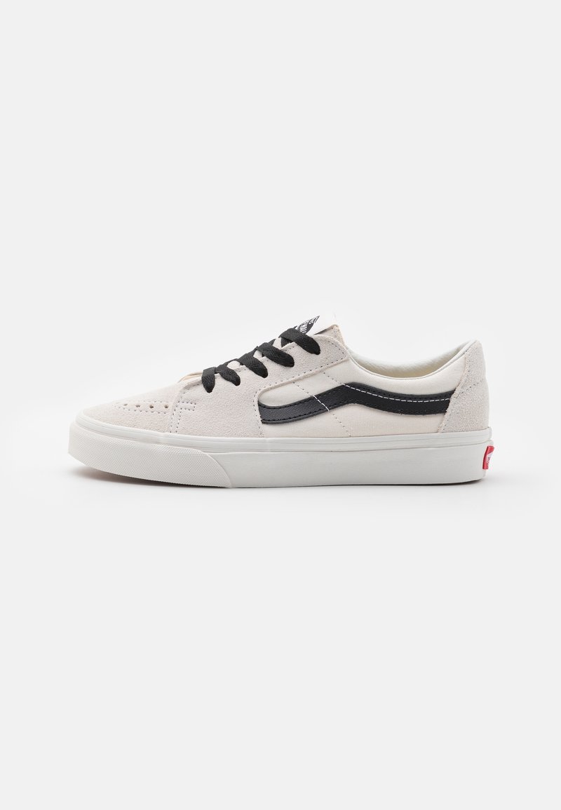 Beige-weißer Sneaker mit niedriger Schnürung, schwarzen Schnürsenkeln und seitlichem Streifen, weißer Gummisohle und rotem Logo an der Ferse vor weißem Hintergrund.