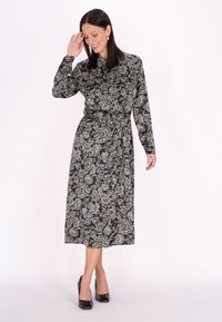 Czarna sukienka z długim rękawem w biały wzór paisley. Midi długość, z paskiem w talii i luźnym krojem, zestawiona z czarnymi szpilkami.