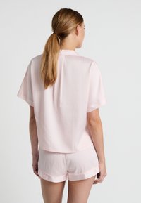 Completo pigiama rosa a maniche corte con un piccolo motivo geometrico. Tessuto liscio, top corto e pantaloni coordinati con orli arrotolati.