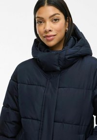 Tumedate sinine täispuhutud jakk, millel on kõrge kaelus, pehme õmblusega disain, paks polsterdus ja mugav lõige. Sujuv tekstuur ilma nähtava riistvaraeta.