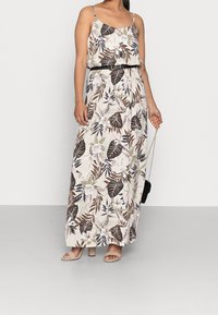 Maxi šaty s tenkými ramínky, s květinovým a listovým vzorem v hnědých, krémových a zelených tónech. Se páskem v pase a hladkým textilním povrchem.