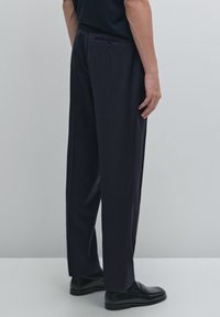 Dark navy tailored trousers with a straight leg design, featuring a single back pocket and subtle texture. Worn with black loafers.