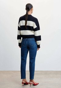 Pull en tricot rayé noir et blanc, coupe ample, manches longues. Associé à un jean bleu taille haute et des escarpins rouges à bride arrière.