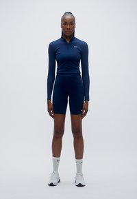 Ensemble de sport bleu marine comprenant un haut manches longues avec une demi-fermeture éclair et un short assorti. Logo Nike blanc sur le haut. Design texturé et ajusté.