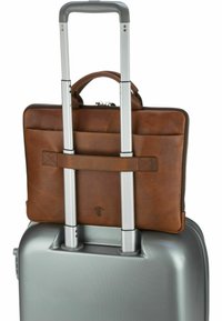 Brun læder laptop taske placeret på en sølvfarvet hårdskal kuffert med struktureret overflade. Teleskophåndtag synligt bag bagagen.