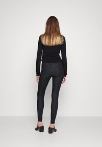 Top negro de manga larga combinado con unos jeans skinny de mezclilla oscura. El conjunto presenta una textura suave y un diseño minimalista, complementado con unos tacones gruesos negros.