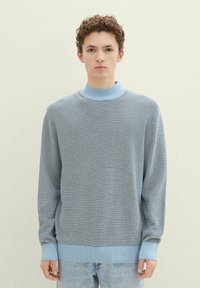 Niebieski sweter w paski, wykonany na drutach, z wysokim ściągaczem i długimi rękawami, charakteryzujący się miękką teksturą i luźnym krojem.