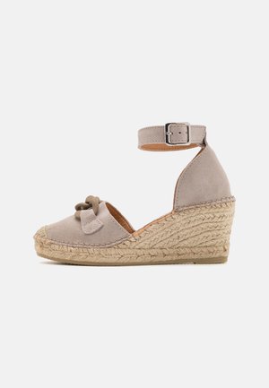 Sandale à semelle compensée en suède gris clair, avec un détail en nœud, une sangle à la cheville avec boucle et un intermédiaire en jute tissé. Semelle en caoutchouc plate.
