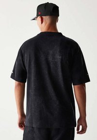 Czarna koszulka o luźnym kroju, krótki rękaw i teksturowana powierzchnia. Posiada detale z logo na lewym rękawie.