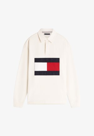 Polo majica dugih rukava u krem boji s tamnoplavim i crvenim logotipom na zakrpi na kojem piše "TOMMY HILFIGER." Ima ovratnik s ovratnikom i rebraste manžete.