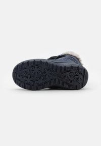 Suela de bota de goma negra con patrones de agarre texturizados, incluidos motivos de flores y surcos profundos para tracción, con un suave ribete de pelo a lo largo de la parte superior.