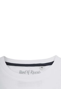 Hvid bomulds-T-shirtkrave med grå indvendig kant og et mærke med teksten "Band of Rascals" i grå tekst. Glat tekstur.