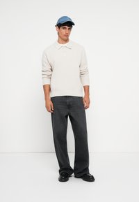 Light beige knitted sweater with a collar, paired with dark gray wide-leg jeans and black shoes. The cap is light blue.
