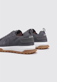 Zapatillas deportivas de un gris oscuro con parte superior de malla, suela de goma con tracción marrón y tirador en la parte trasera. Branding "ECOALF" visible en el talón.