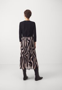 Svart långärmad topp i kombination med en flödande, veckad kjol med ett vågigt mönster i svart och beige, kompletterad med svart stövlar som går upp till knäna.