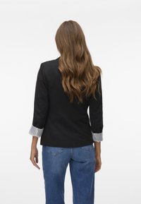 Svart blazer med trekvartslånga ärmar, med ett randigt vit och grått manschett, i kombination med ljusblå denimjeans.