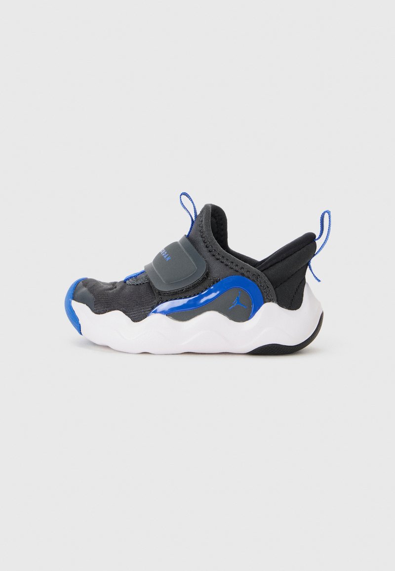 Chaussure de sport noire avec une tige lisse, des accents bleus, une sangle élastique et une semelle blanche texturée. Dispose d'une languette pour un enfilage facile.